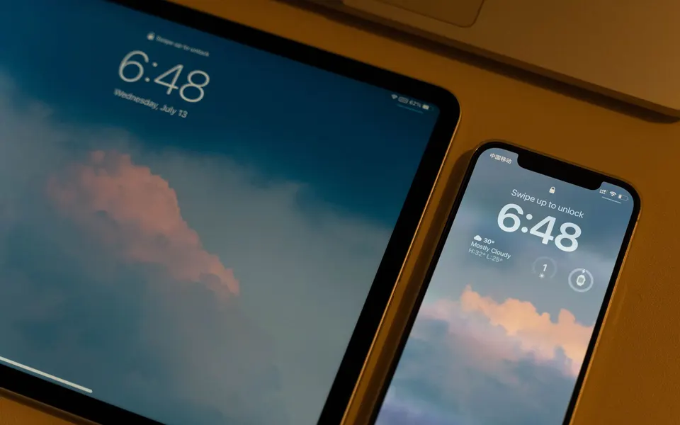 Tablet en smartphone naast elkaar op een houten tafel, allebei met het vergrendelscherm aan